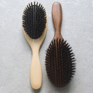 oval beechwood hair brush with black natural bristles set in rubber cushion. side by side of pale beechwood and dark nut oil beechwood brush